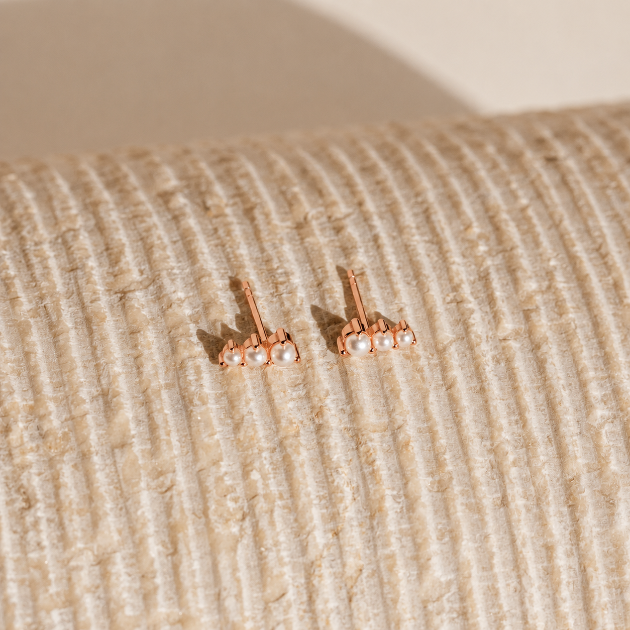 Rose gold earrings with pearls on a textured beige surface